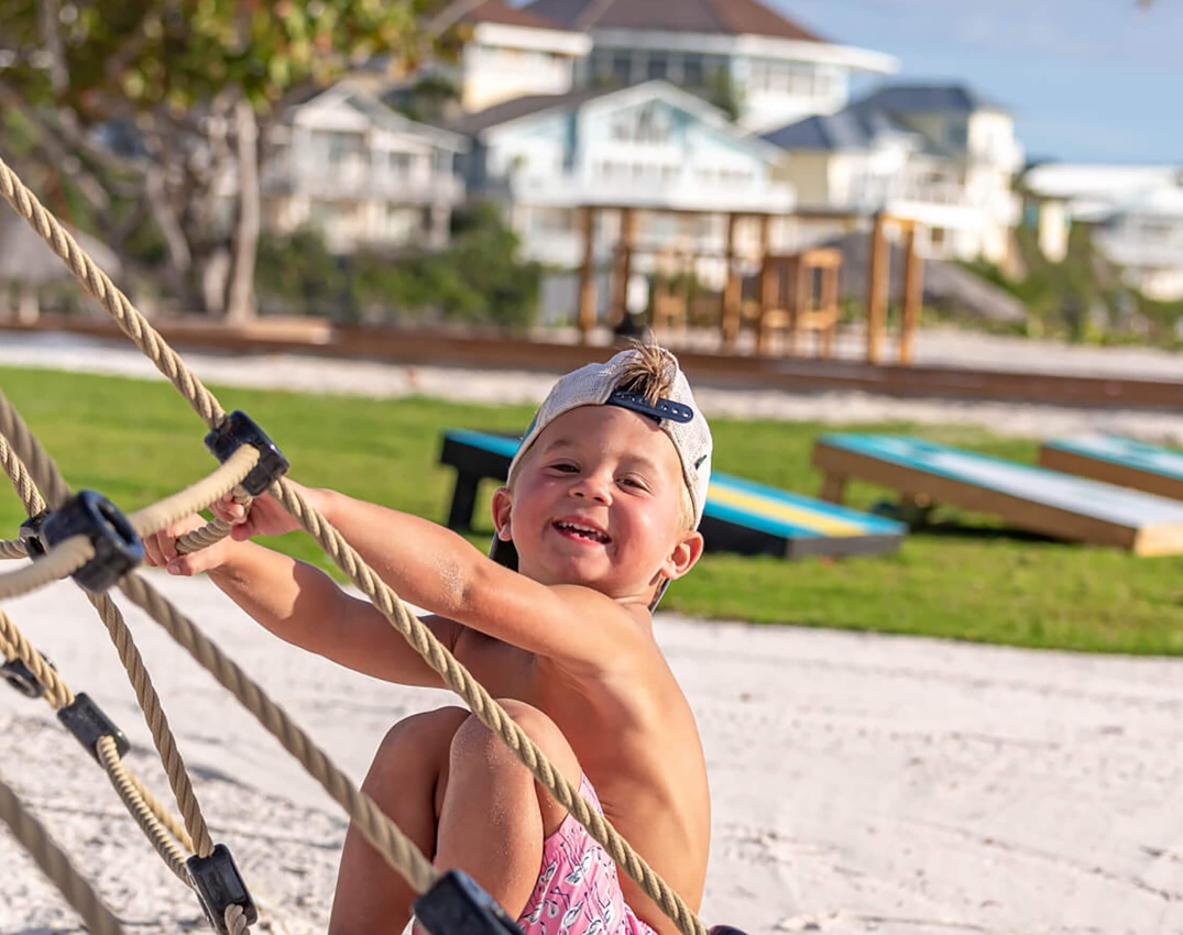 A boy smiling on a beach playground at The Abaco Club