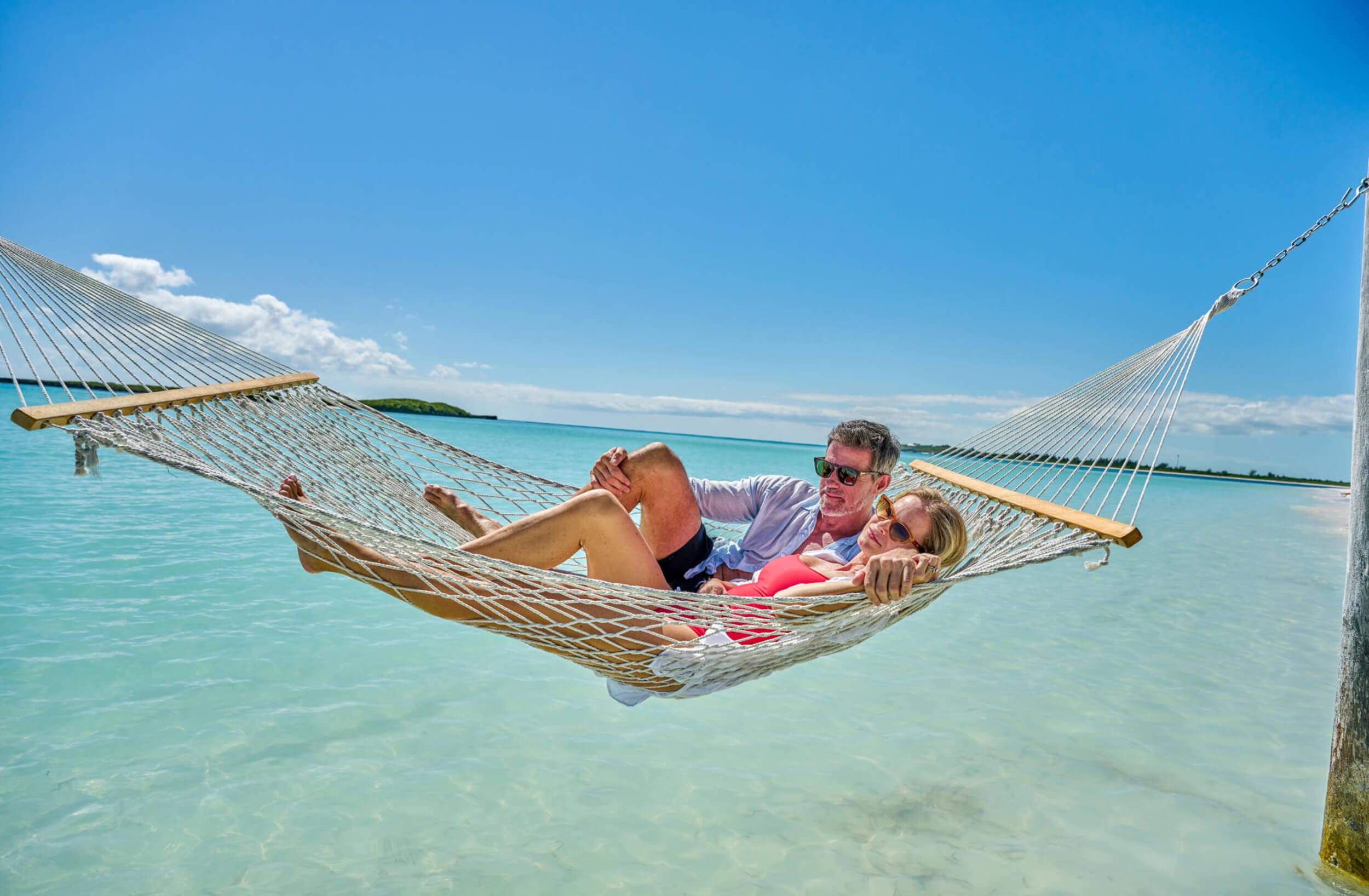 Couple relaxing in a hammock over the water, enjoying the serene coastal living at The Abaco Club