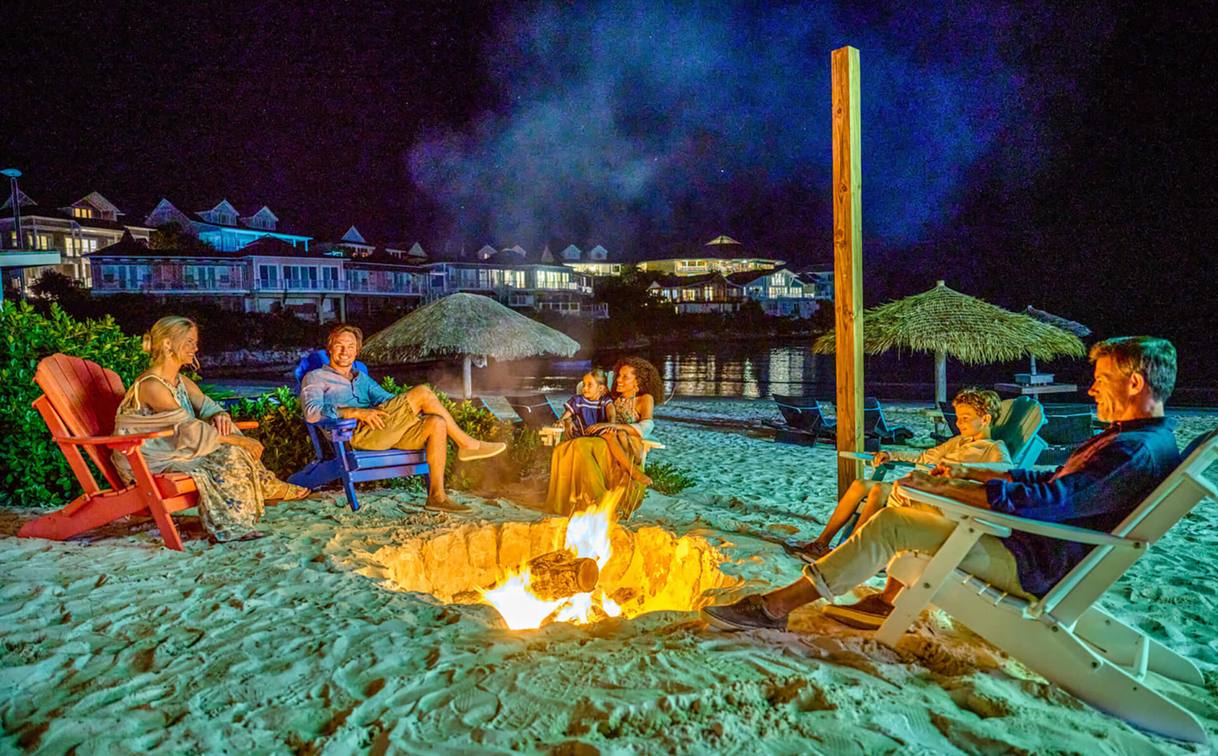 Friends gathered around a beach bonfire at night at The Abaco Club.