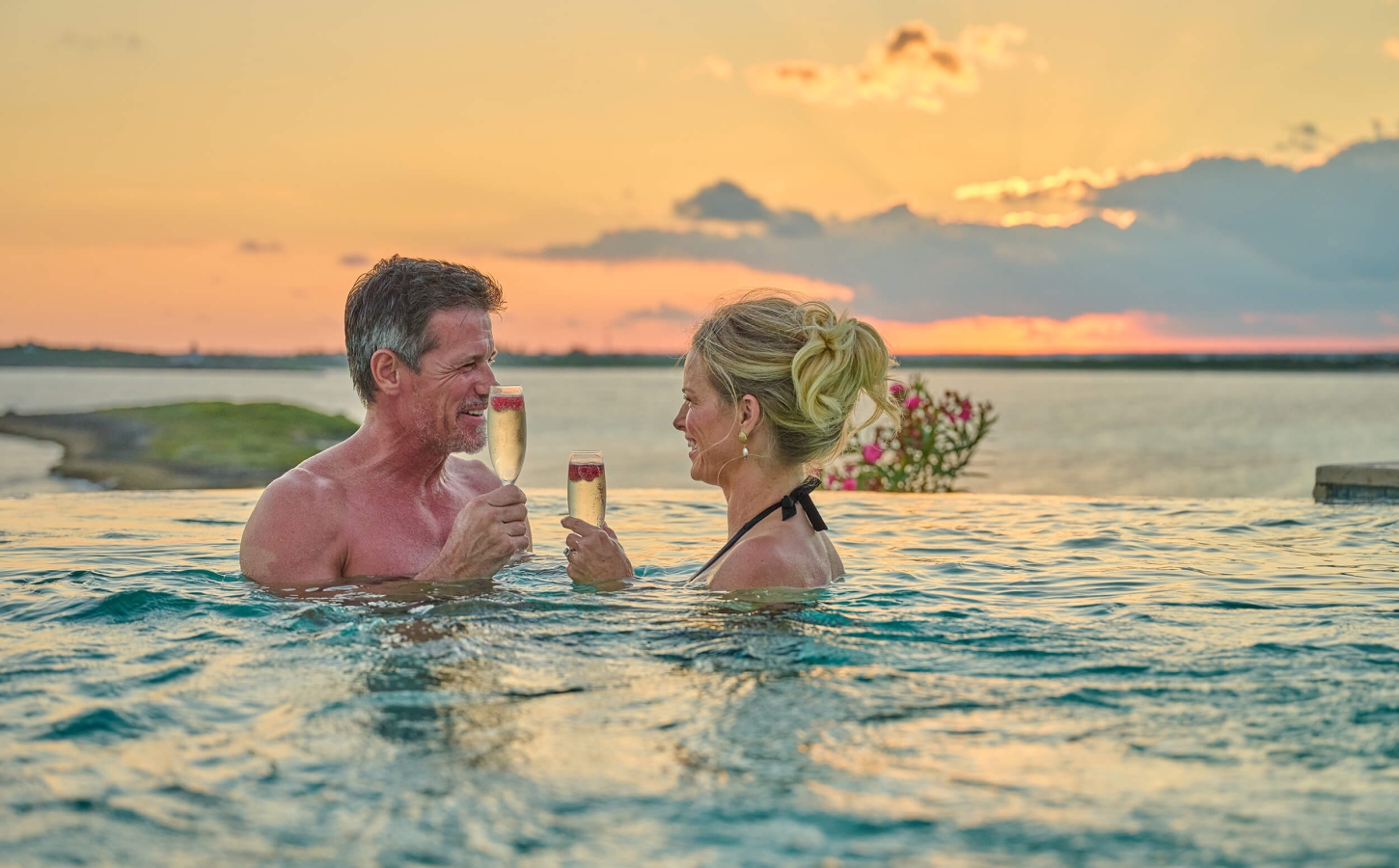 Couple in an infinity pool enjoying a tropical sunset, embodying the romantic club lifestyle at The Abaco Club.