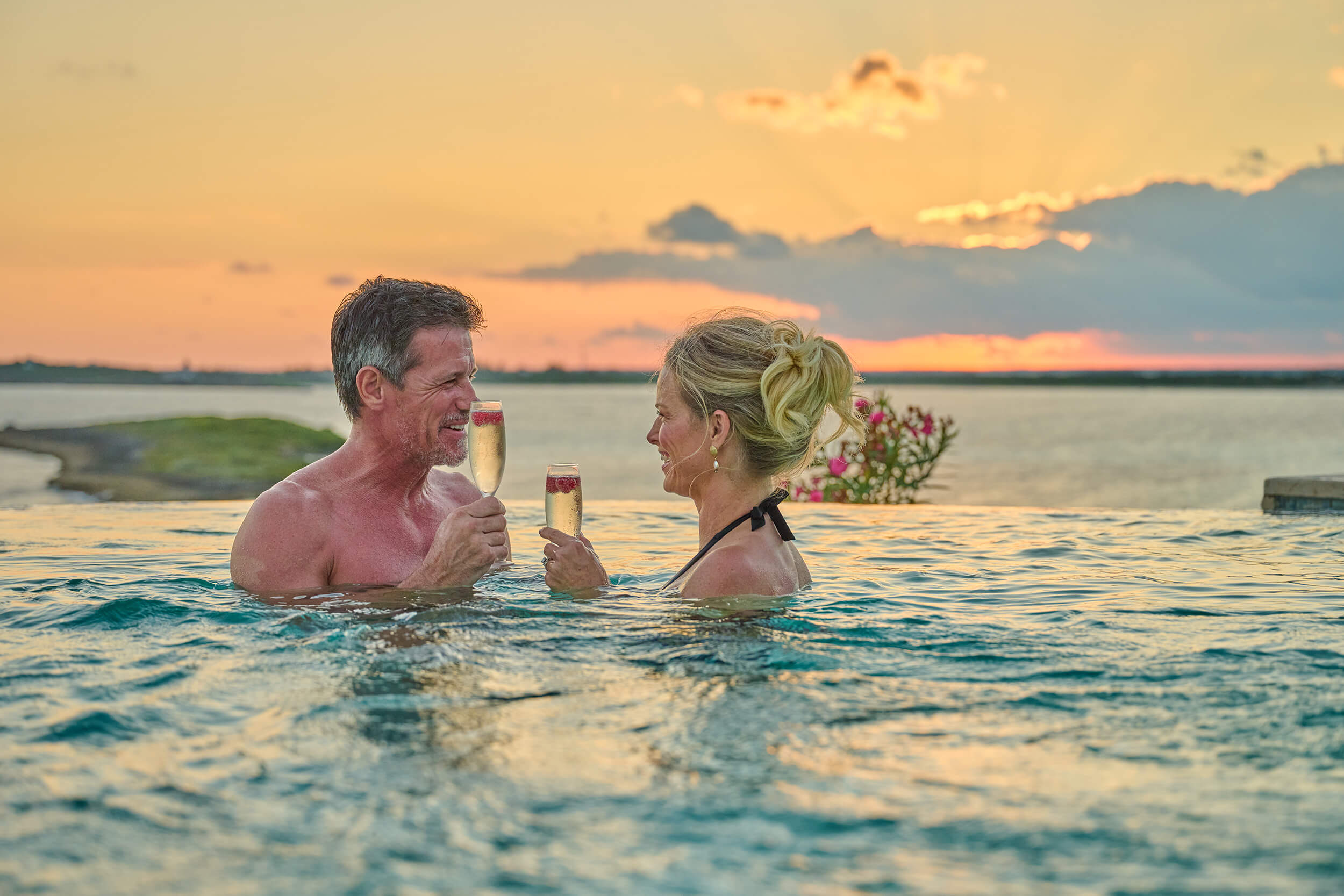 Couple in an infinity pool enjoying a tropical sunset, embodying the romantic club lifestyle at The Abaco Club.