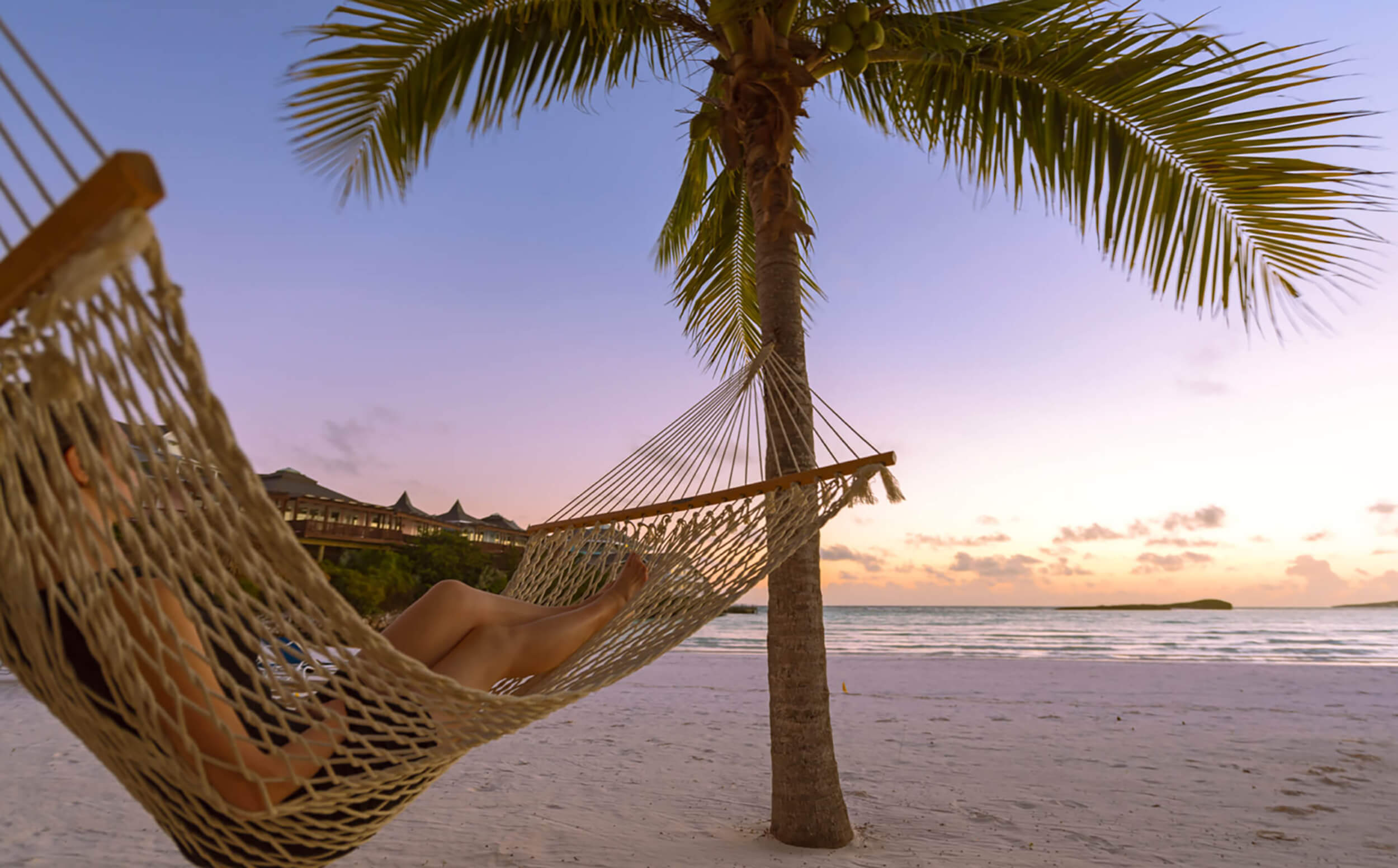 A person lying on a hammock with a sunset view in the background at The Abaco Club