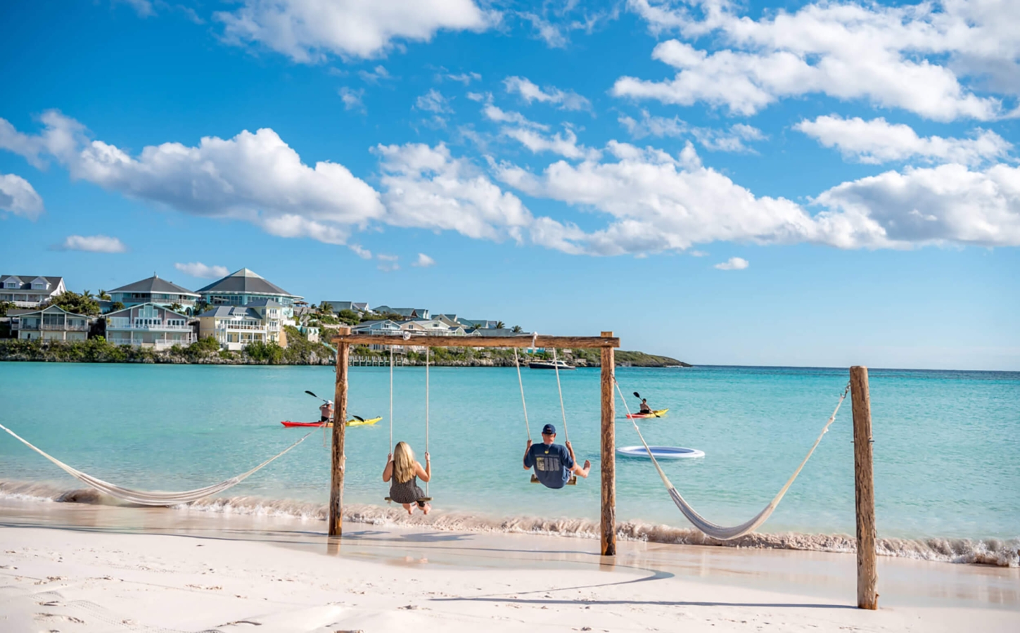 Two people on wooden swings at The Abaco Club offering a leisurely club lifestyle amidst the stunning coastal landscape of the Bahamas.