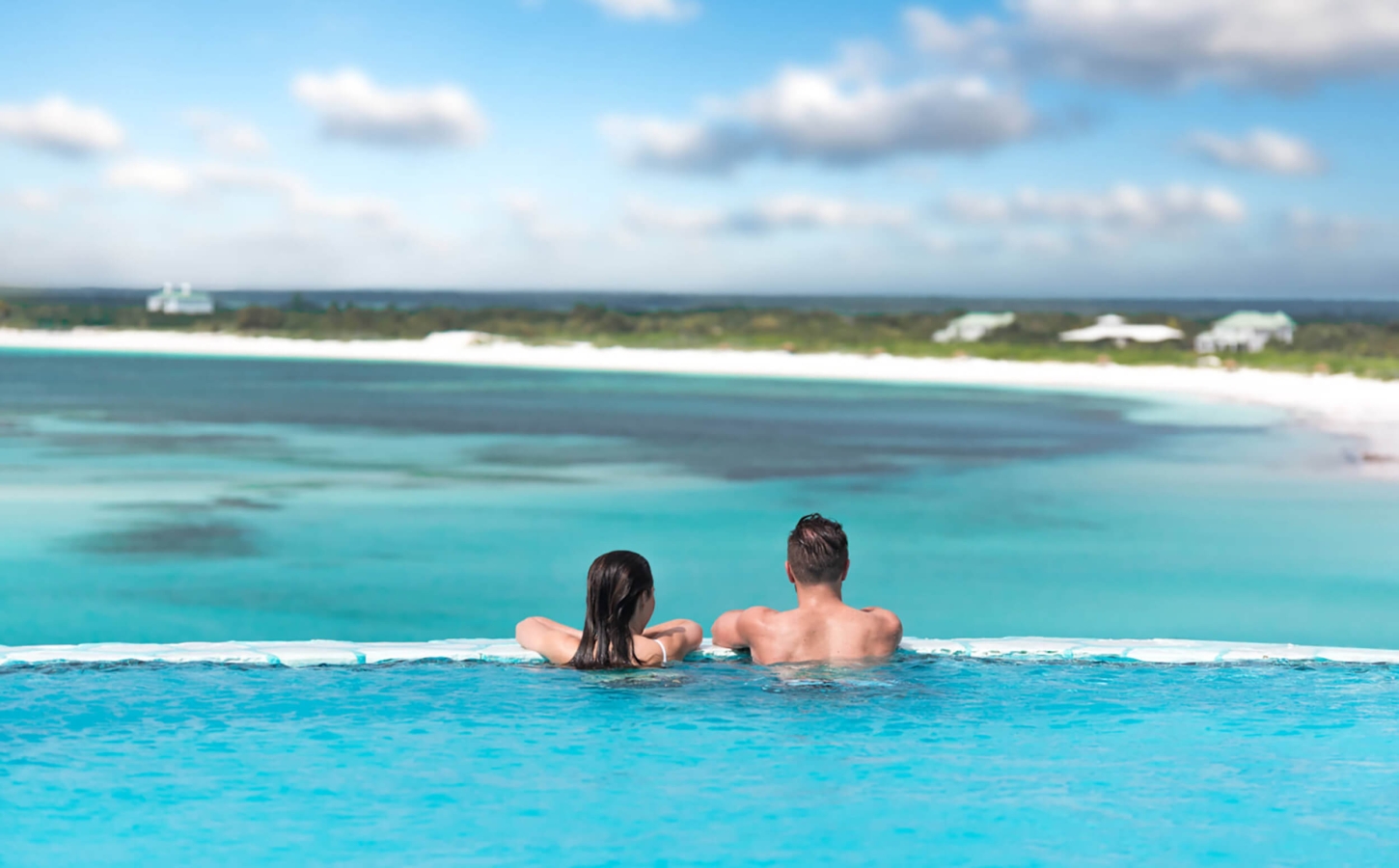 A couple enjoying the infinity pool at The Abaco Club, overlooking the pristine Bahamian coast.