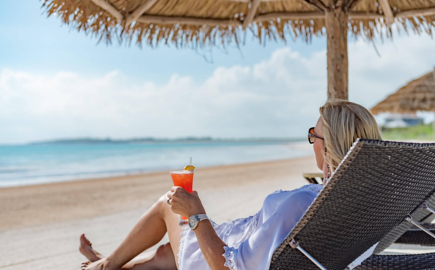 Relaxed club lifestyle at The Abaco Club with a woman enjoying a cocktail on the beach, surrounded by the beauty of The Bahamas.
