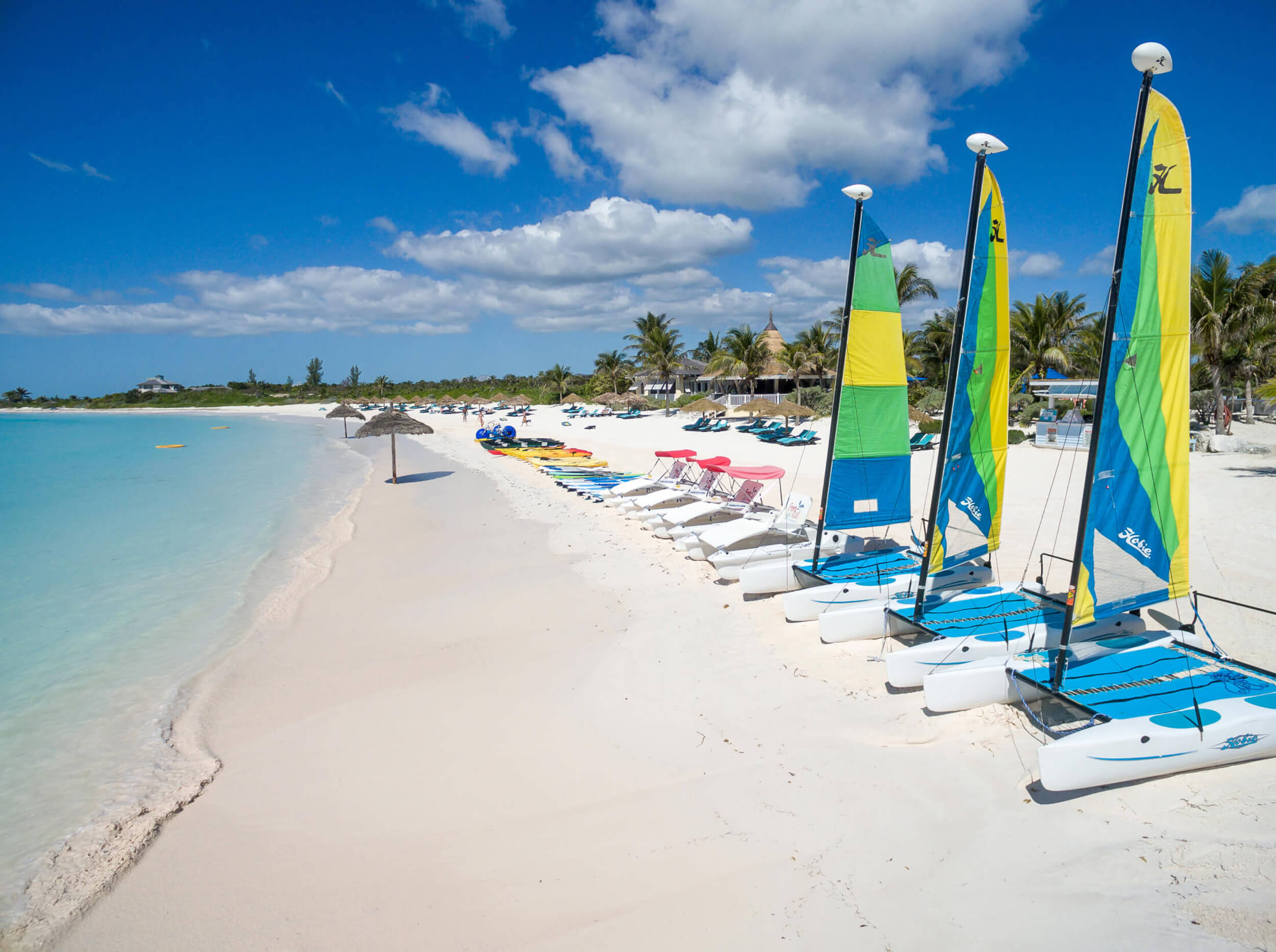 Image of colorful boats and kayaks lined up on the white sands of The Abaco Club beach