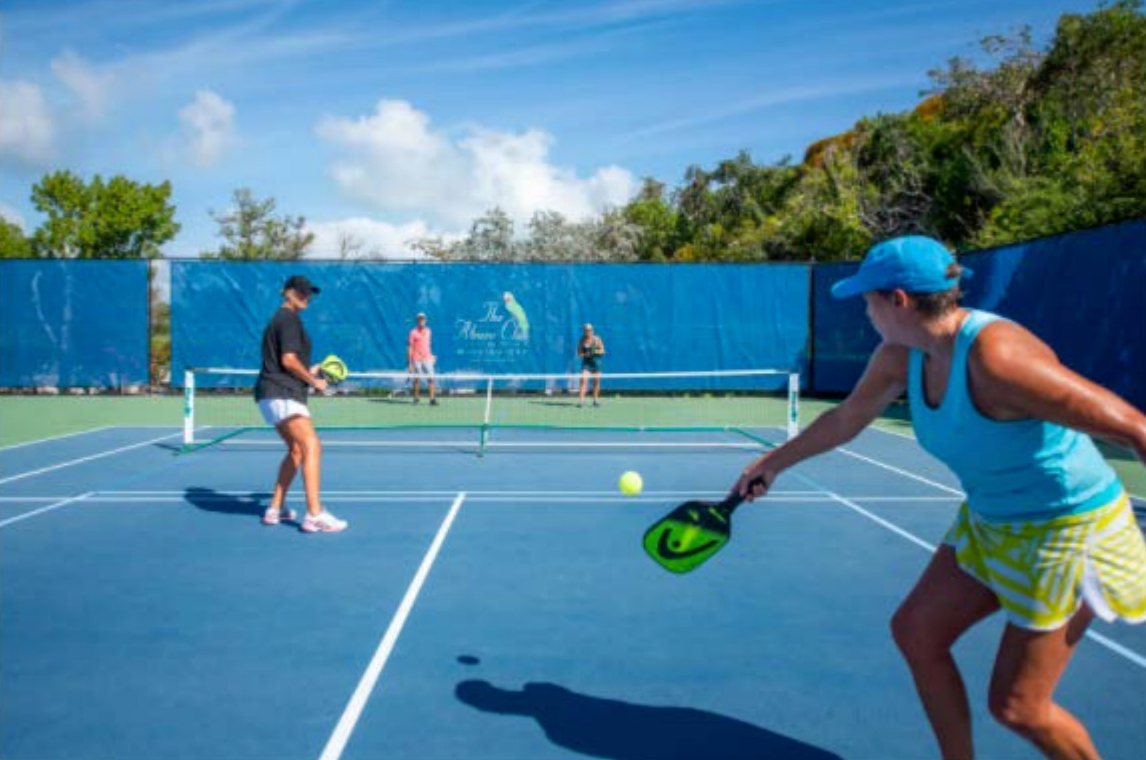 Players engaging in a casual game of tennis at The Abaco Club, with the lush golf course visible in the background, blending sports and coastal living