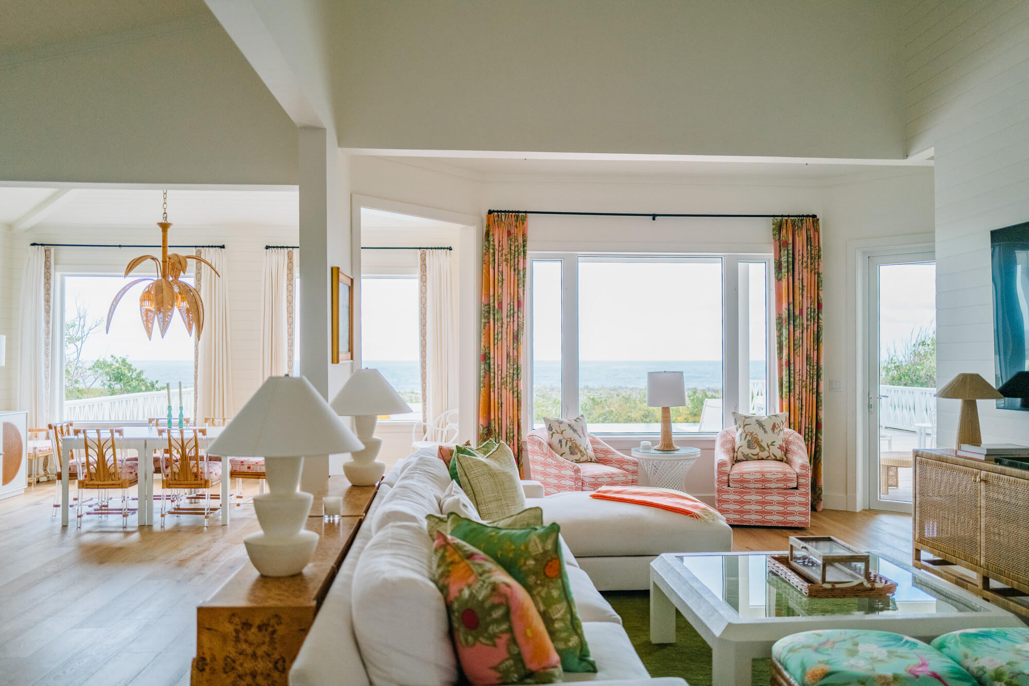 Open-plan living room with white sofas and colorful tropical cushions, large windows showing the beach and ocean view.
