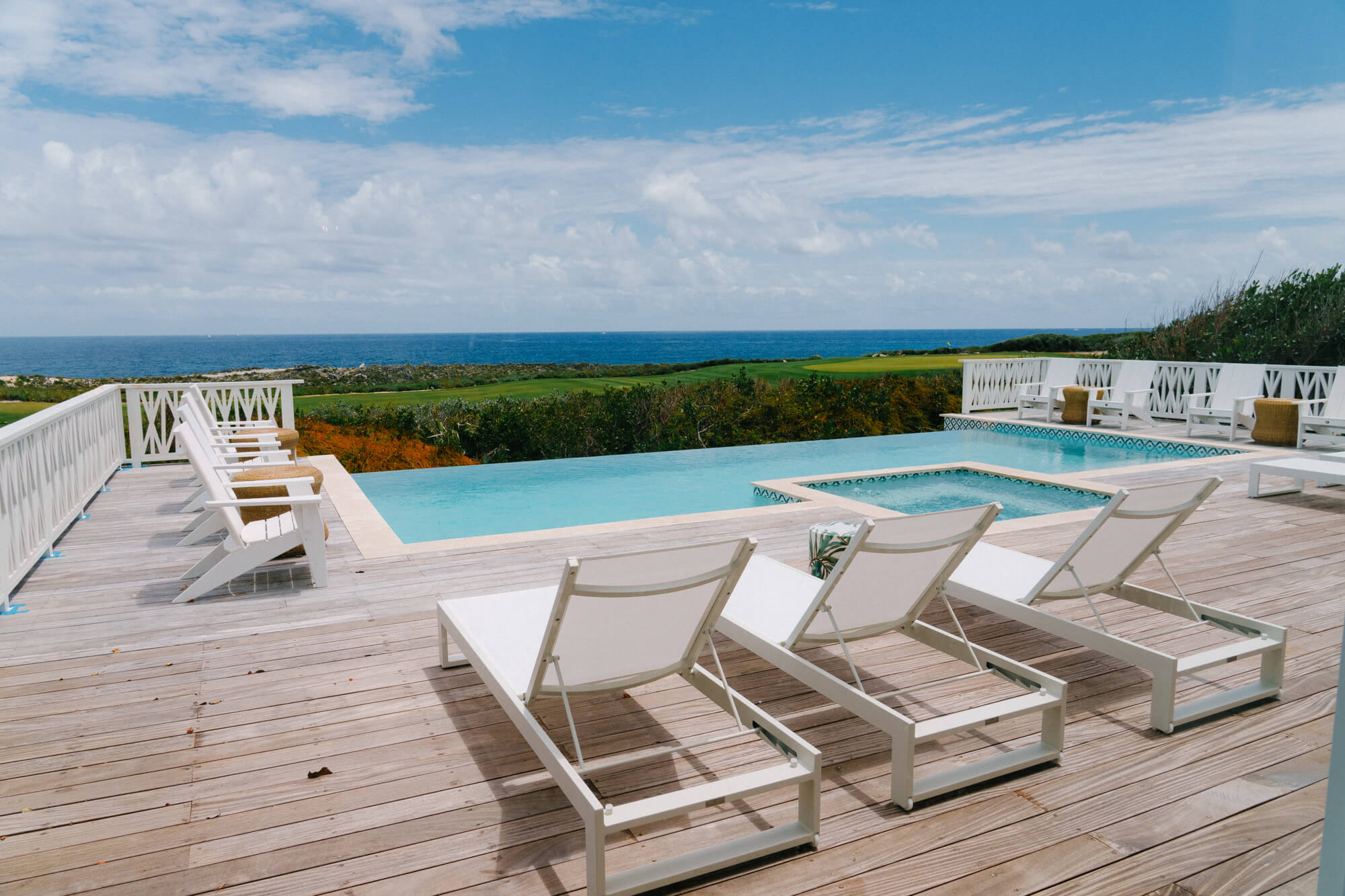 Pool deck with white lounge chairs facing an ocean view under a blue sky.