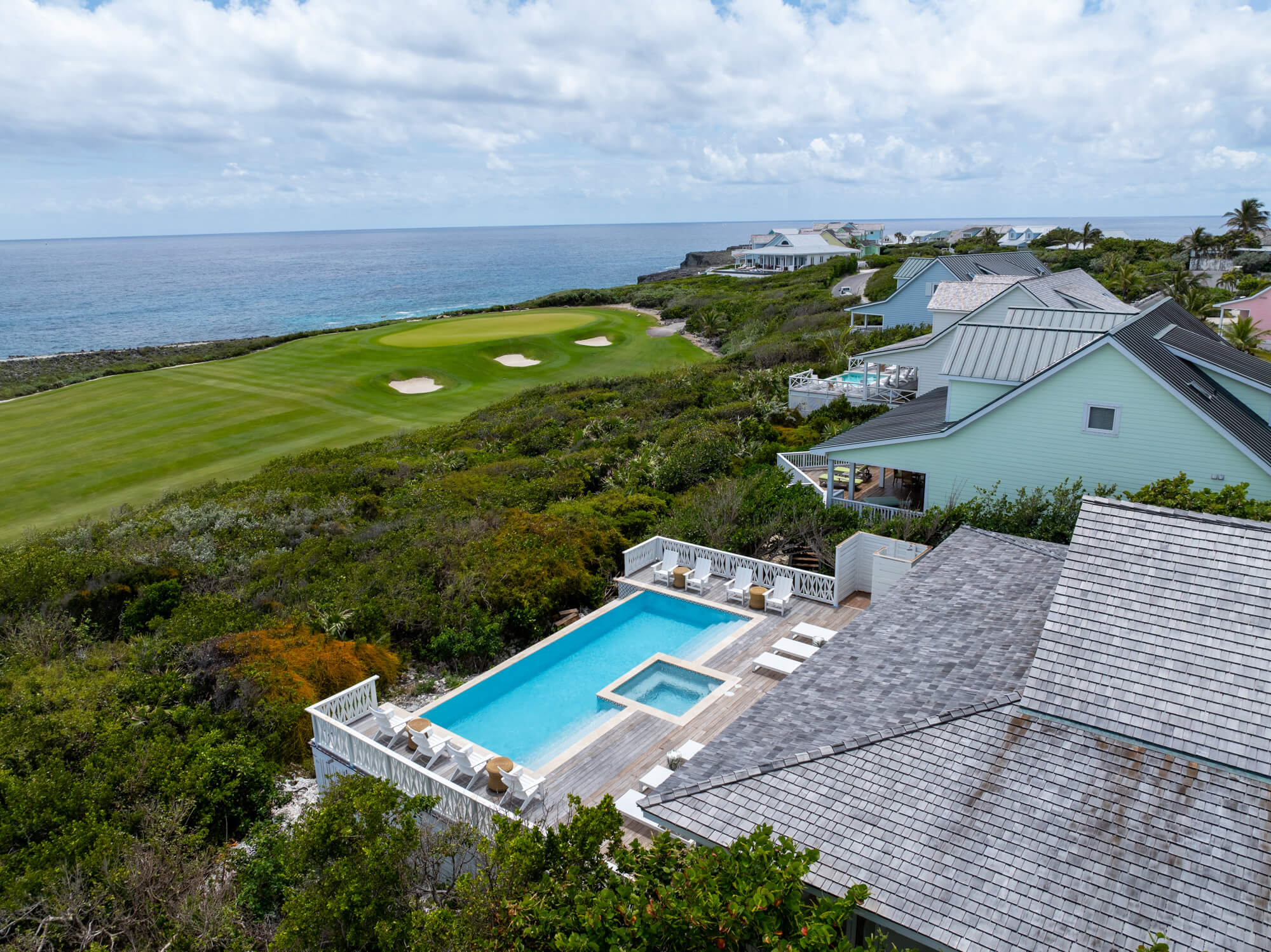 Aerial view of a coastal resort: blue ocean, green golf course with sand bunkers, and pastel beach houses along the shoreline
