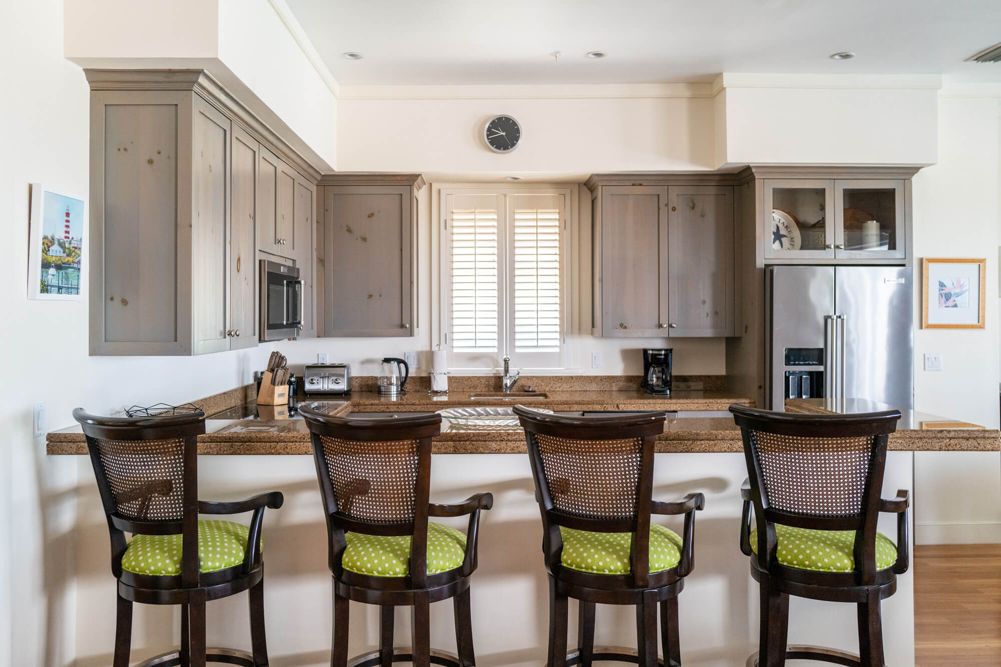 Modern kitchen with grey wooden cabinets, granite island, and four bar stools along a breakfast bar.