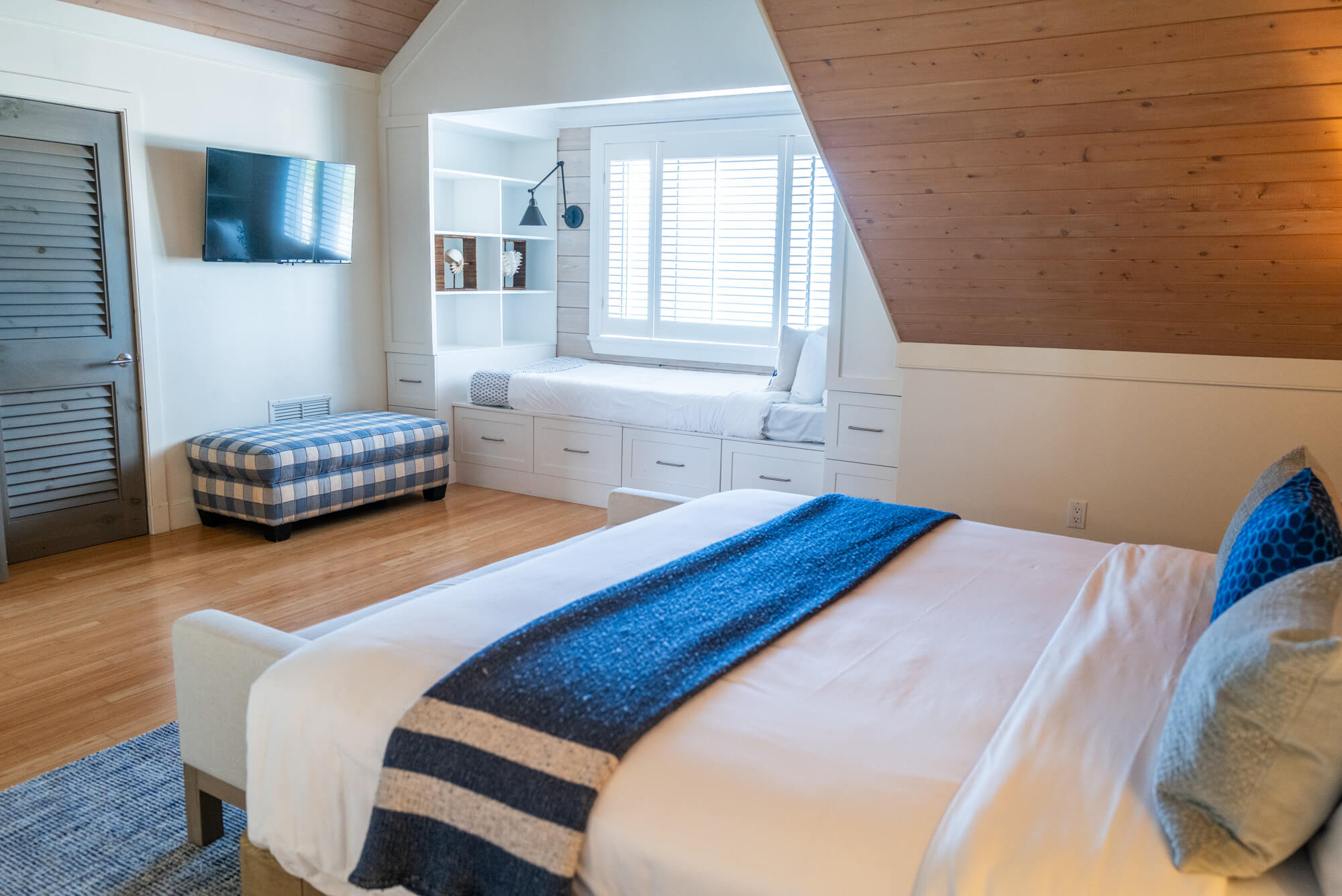 Bedroom with white built-in window seat and storage, a wall-mounted TV, and a blue plaid ottoman.