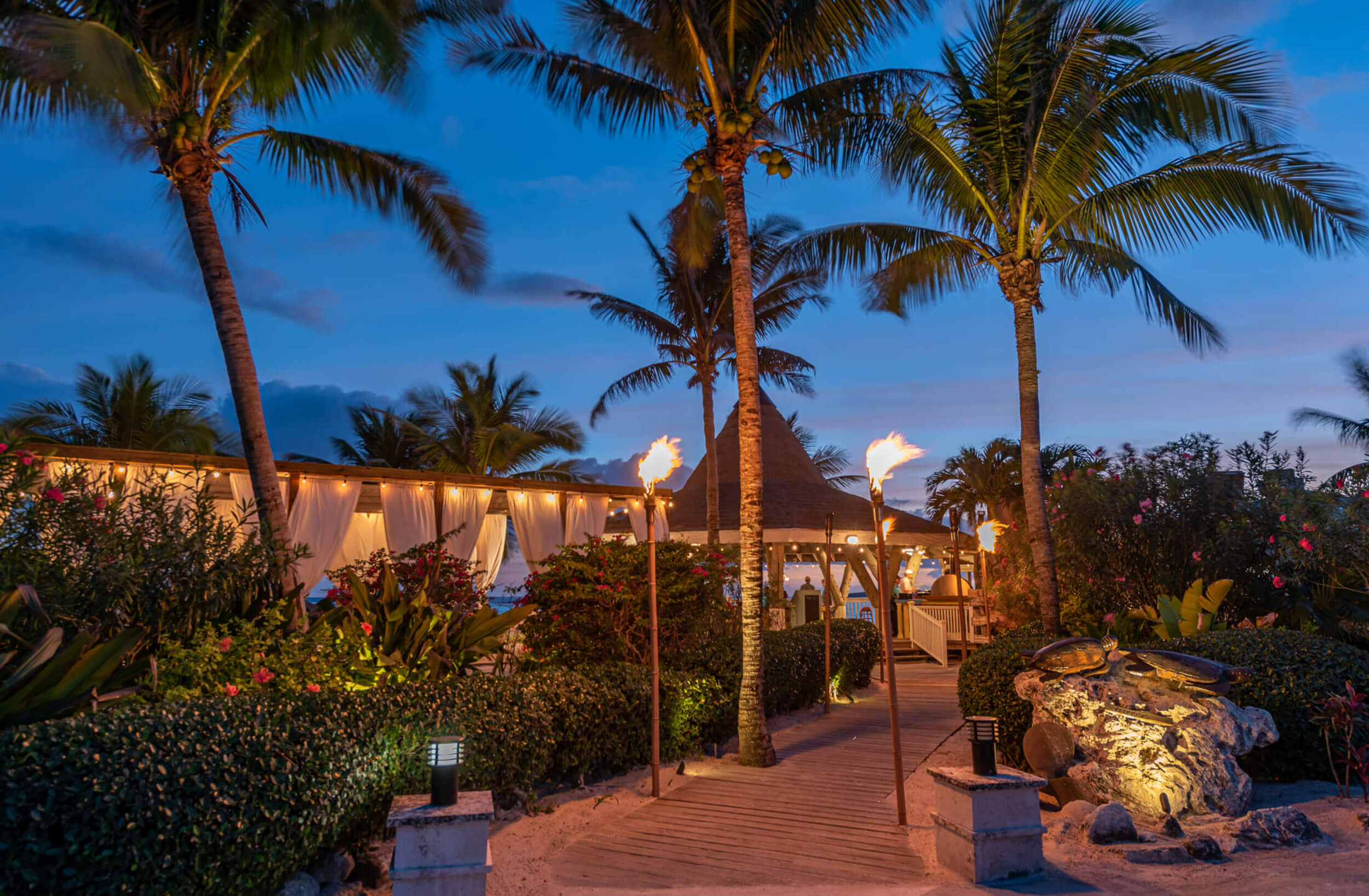 Enchanting evening ambiance at The Abaco Club with torch-lit paths, highlighting upscale coastal living and club amenities