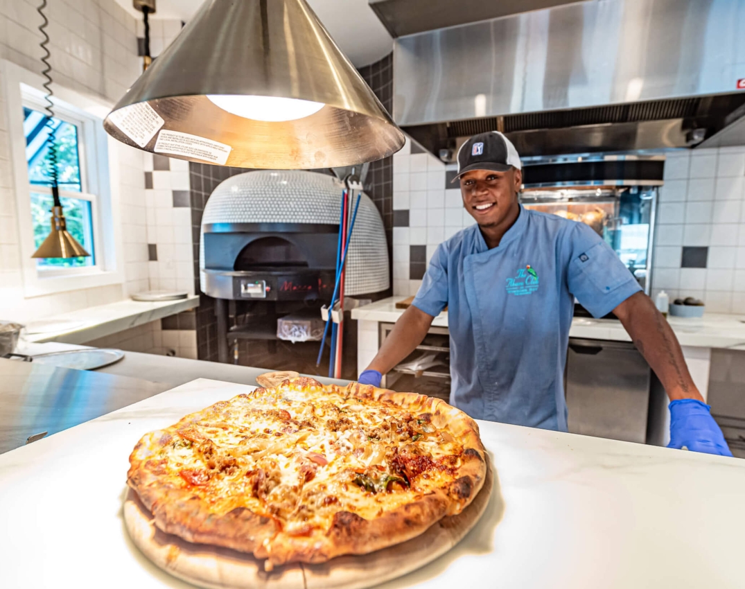 Chef proudly presenting a freshly baked pizza at The Abaco Club's beachfront restaurant.
