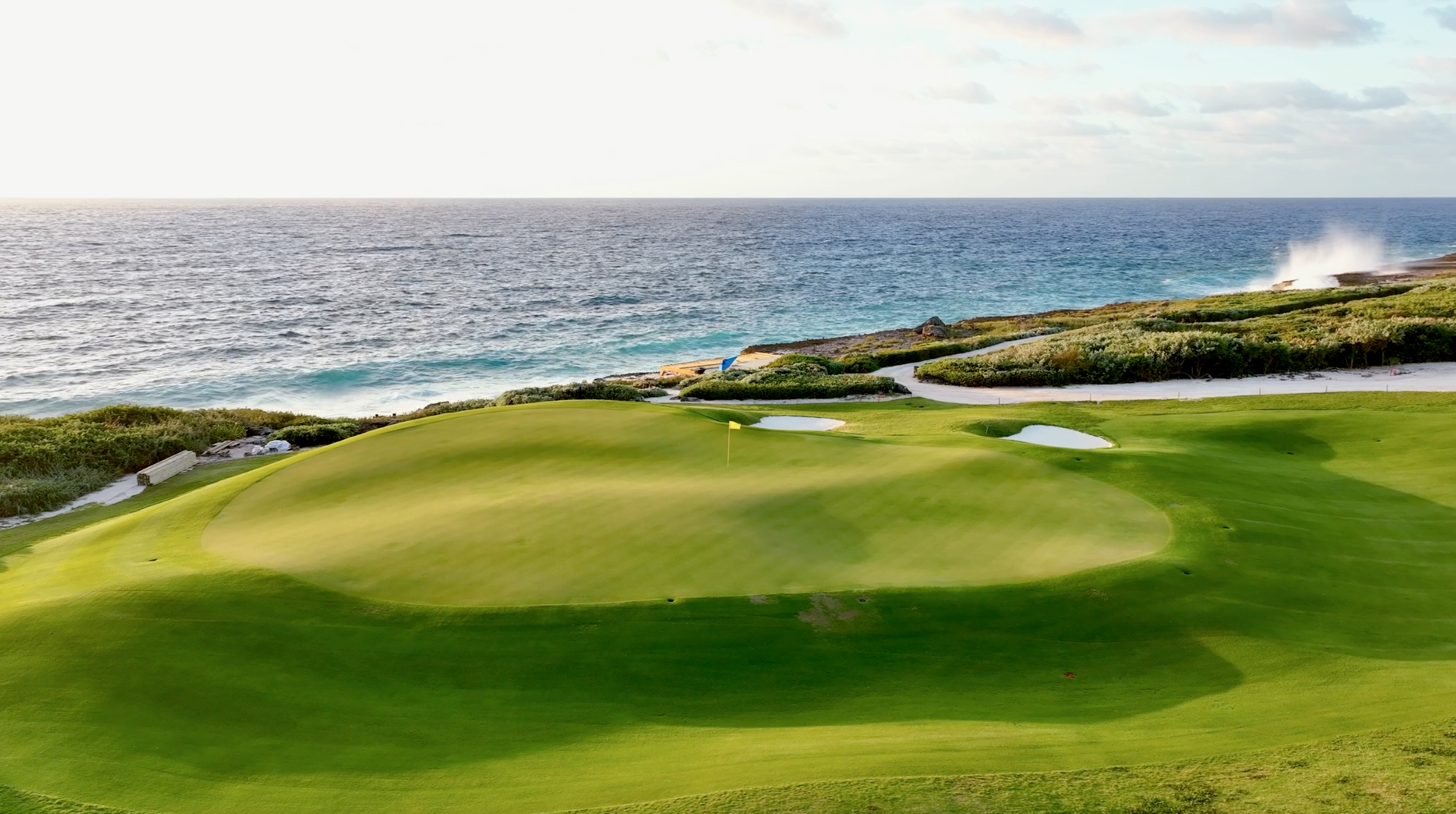 Scenic view of a golf green at The Abaco Club with ocean spray in the background, blending sport and the natural beauty of the Bahamas
