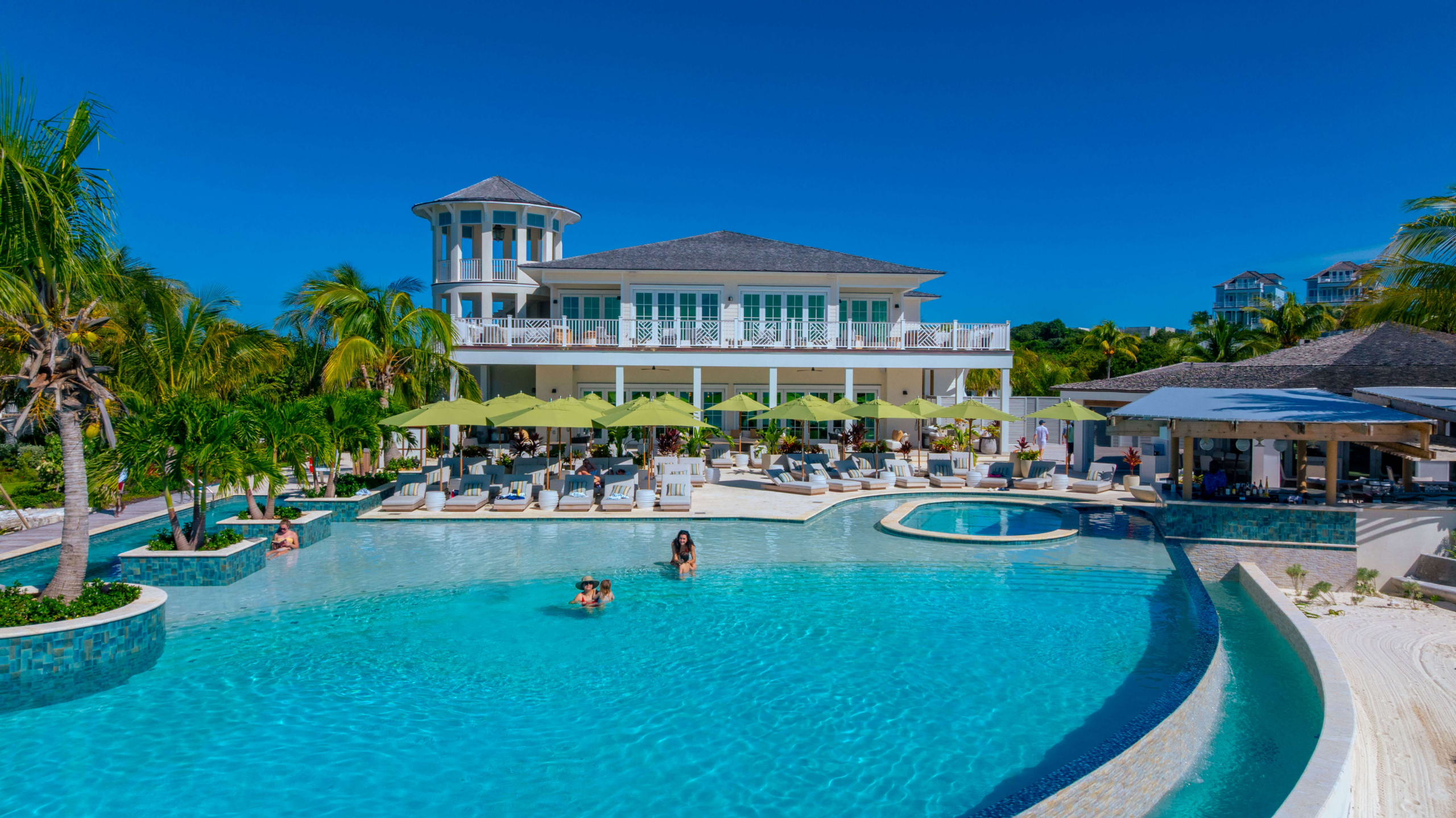 Resort pool area with turquoise water, lime umbrellas, sun loungers, and a white multi‑level building in the background.