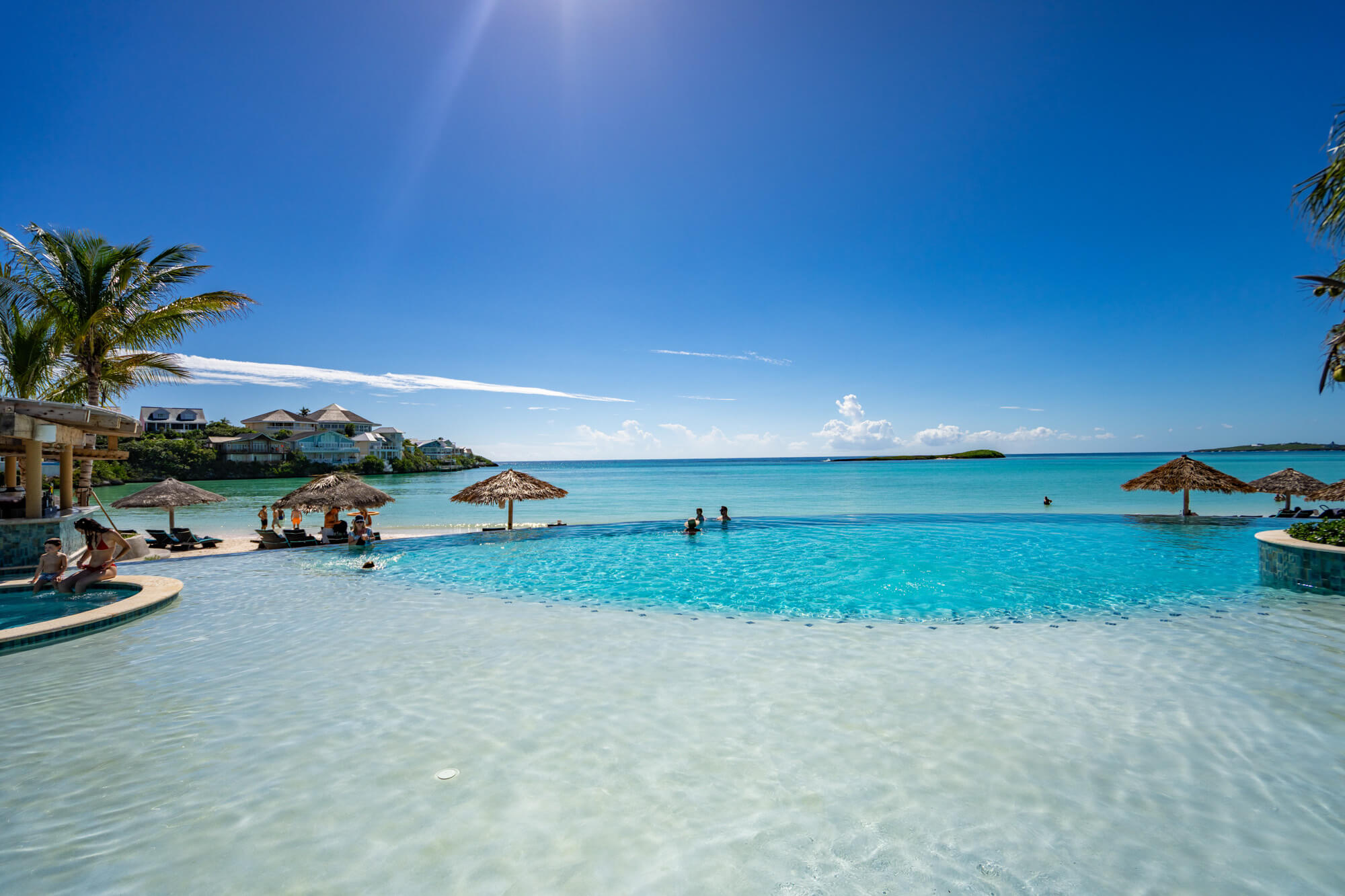 Tropical beach resort with a turquoise pool, palm trees, and a bright blue sky.
