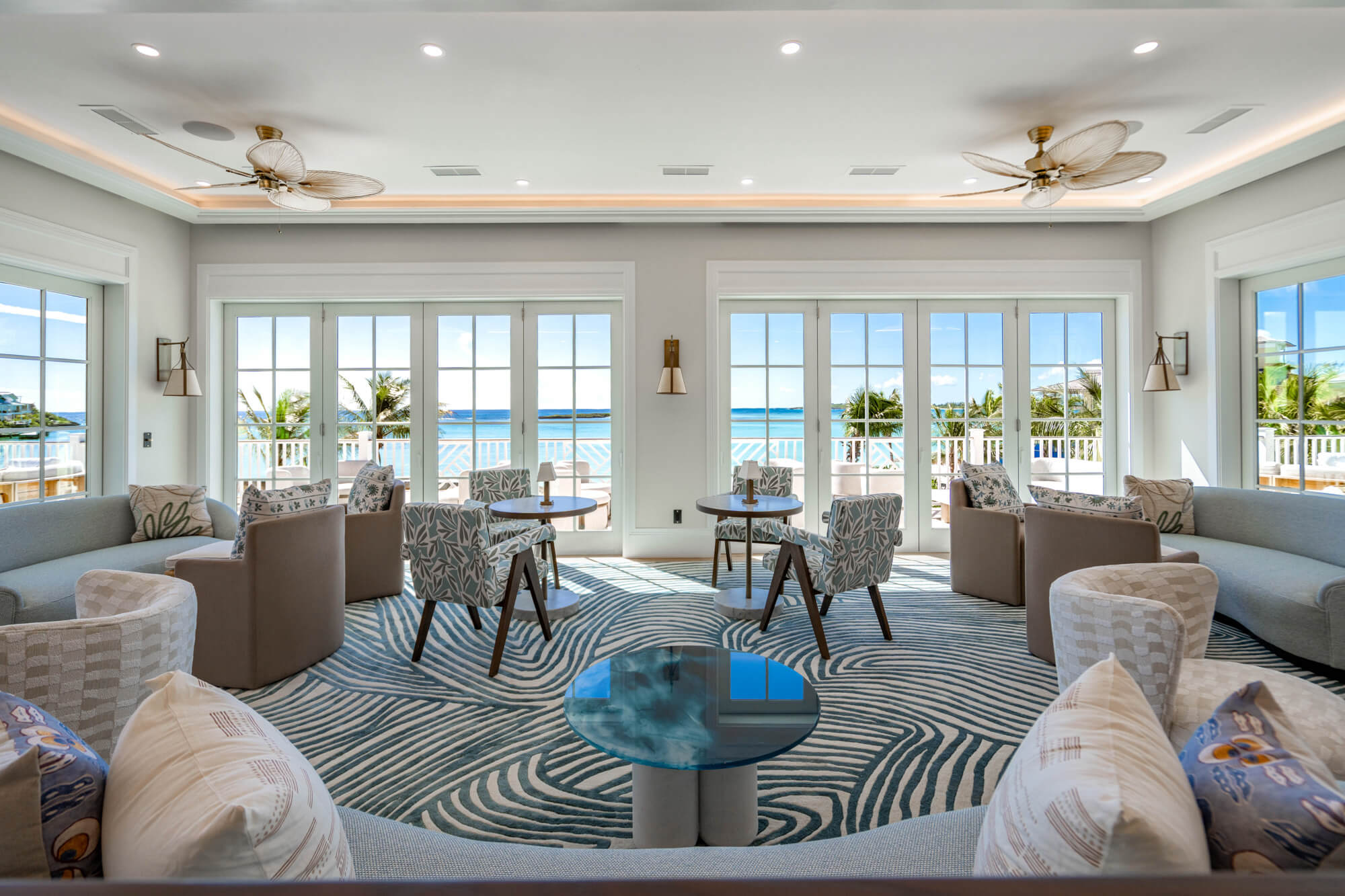 Coastal living room with glass doors opening to an ocean view, cushioned seating, and a blue striped rug.