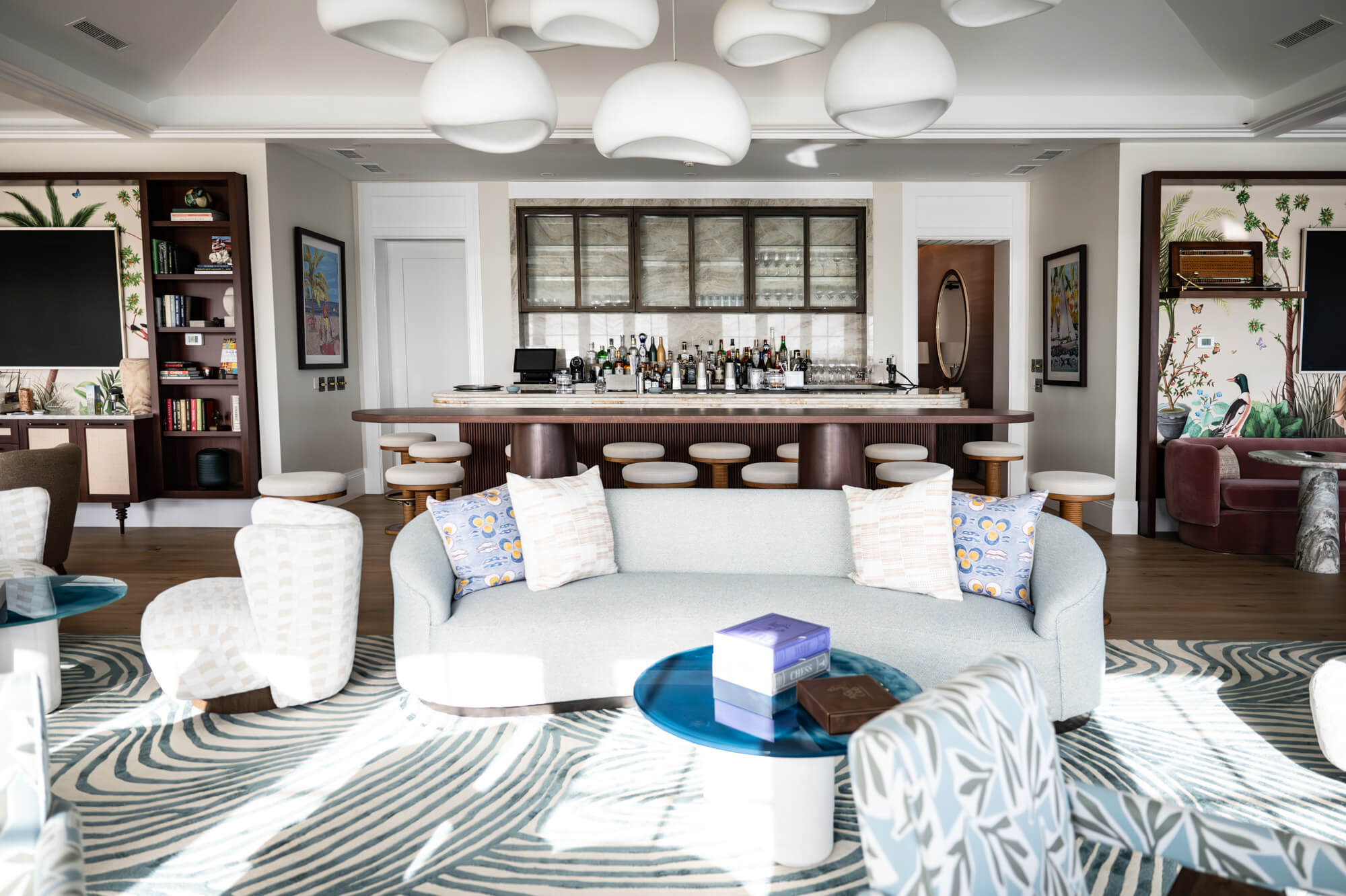 Open-plan living room with a marble-topped bar, zebra-striped rug, and tropical-patterned walls; seating and coffee tables throughout.