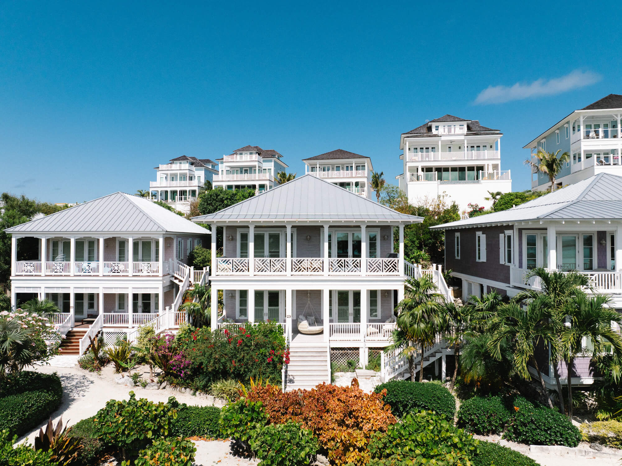 Row of white seaside townhouses with balconies under a clear blue sky, tropical garden in foreground