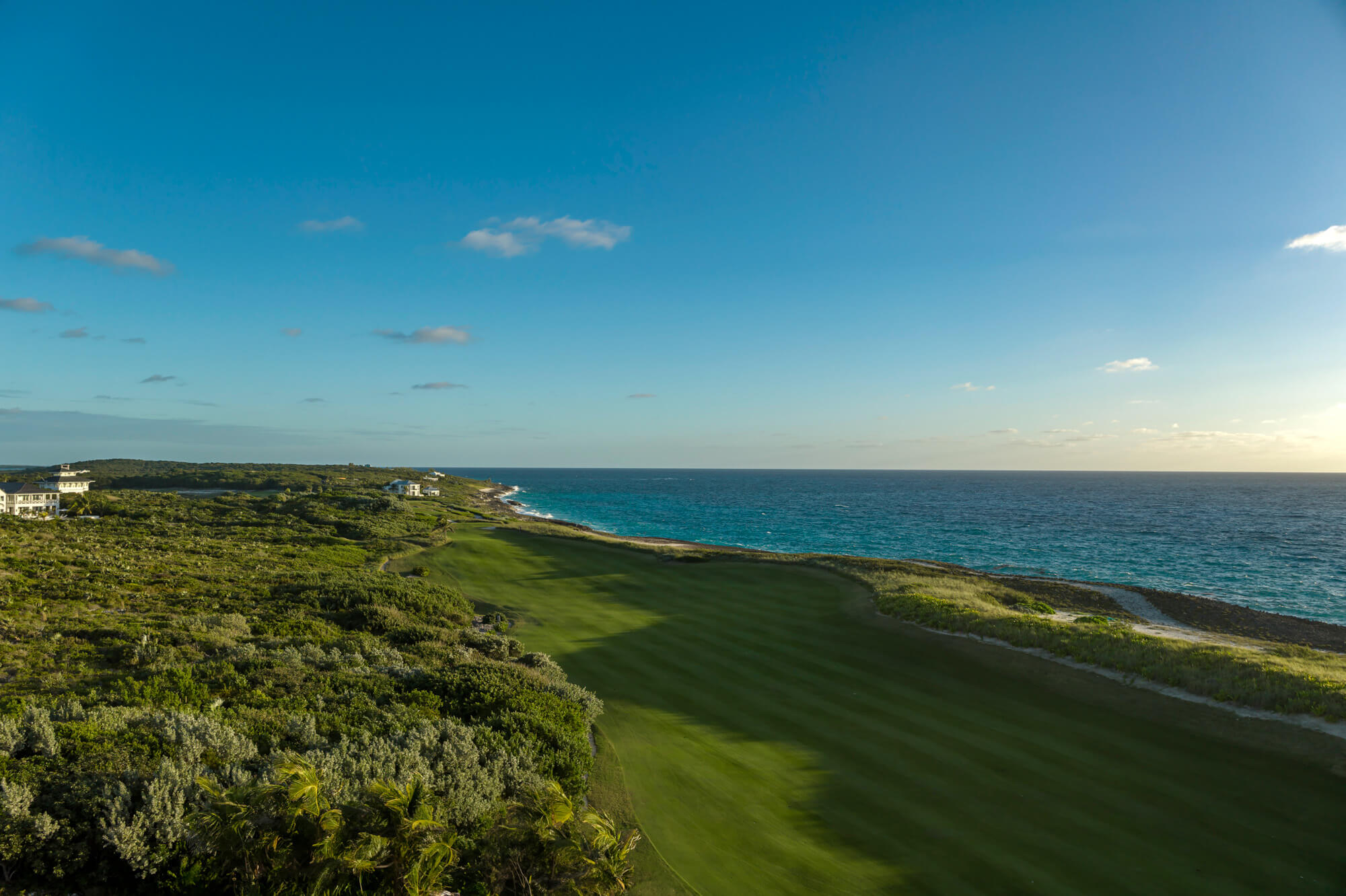 Aerial view of a coastal golf course with green fairways meeting the blue ocean on the horizon.