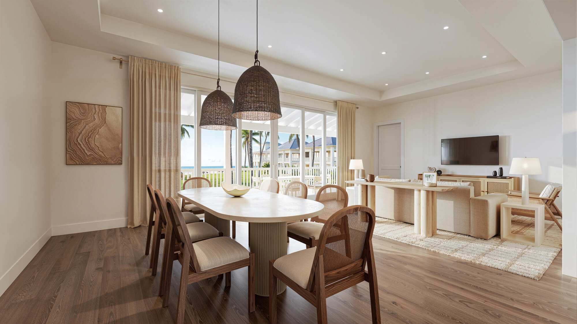 Bright coastal dining and living area with a round wooden table, wicker pendant lamps, and large windows showing palm trees outside.