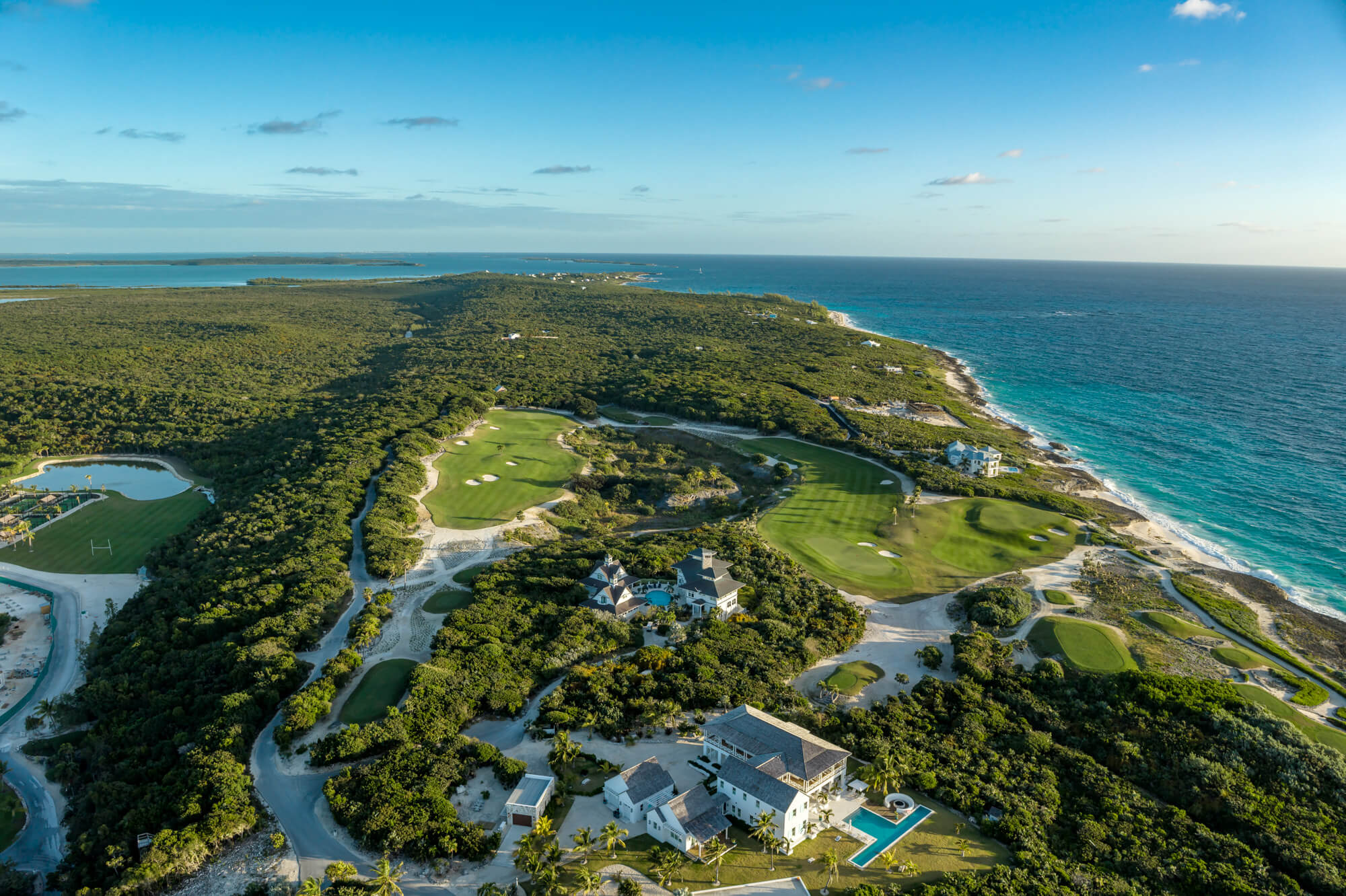 Aerial view of a coastal golf resort with green fairways, sand traps, and the blue ocean along the right edge.